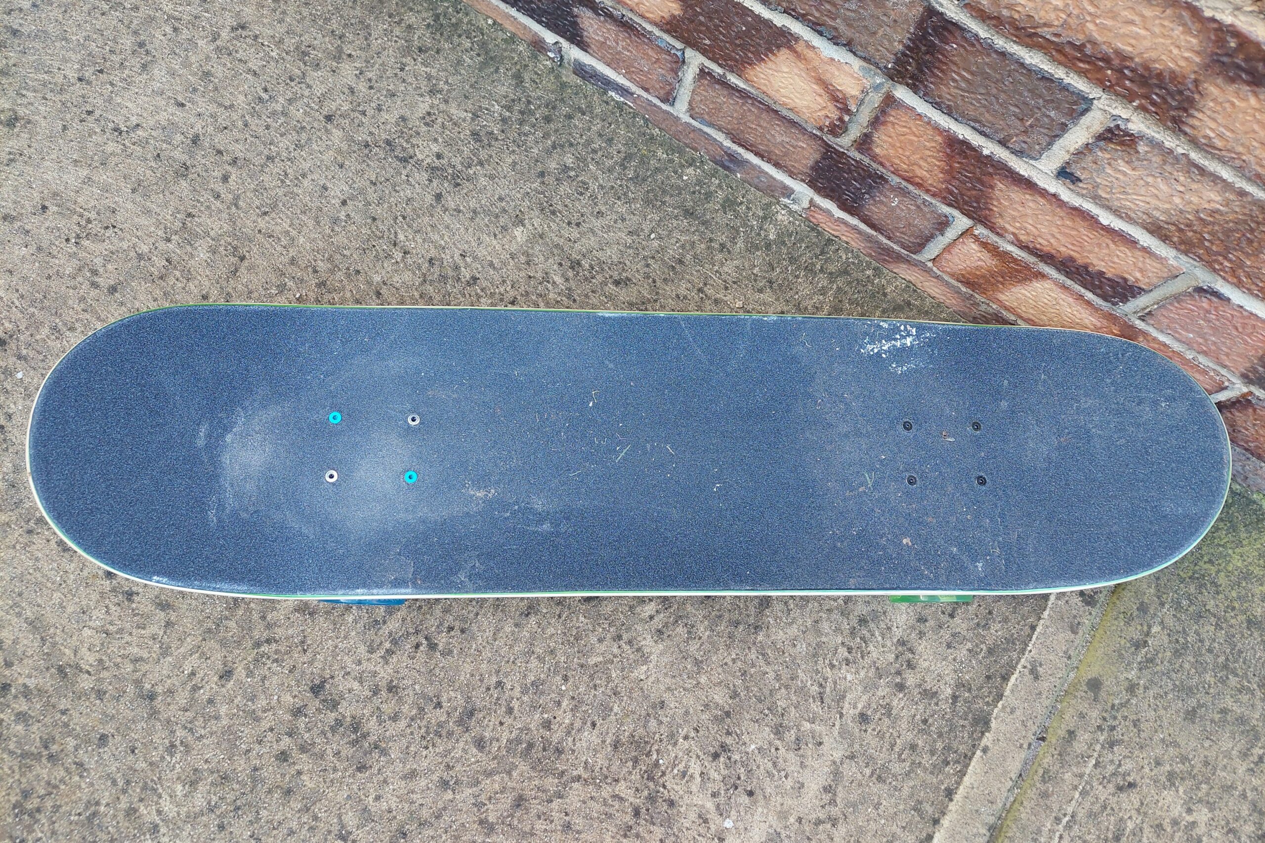 A top-down view of a dirty skateboard on concrete.