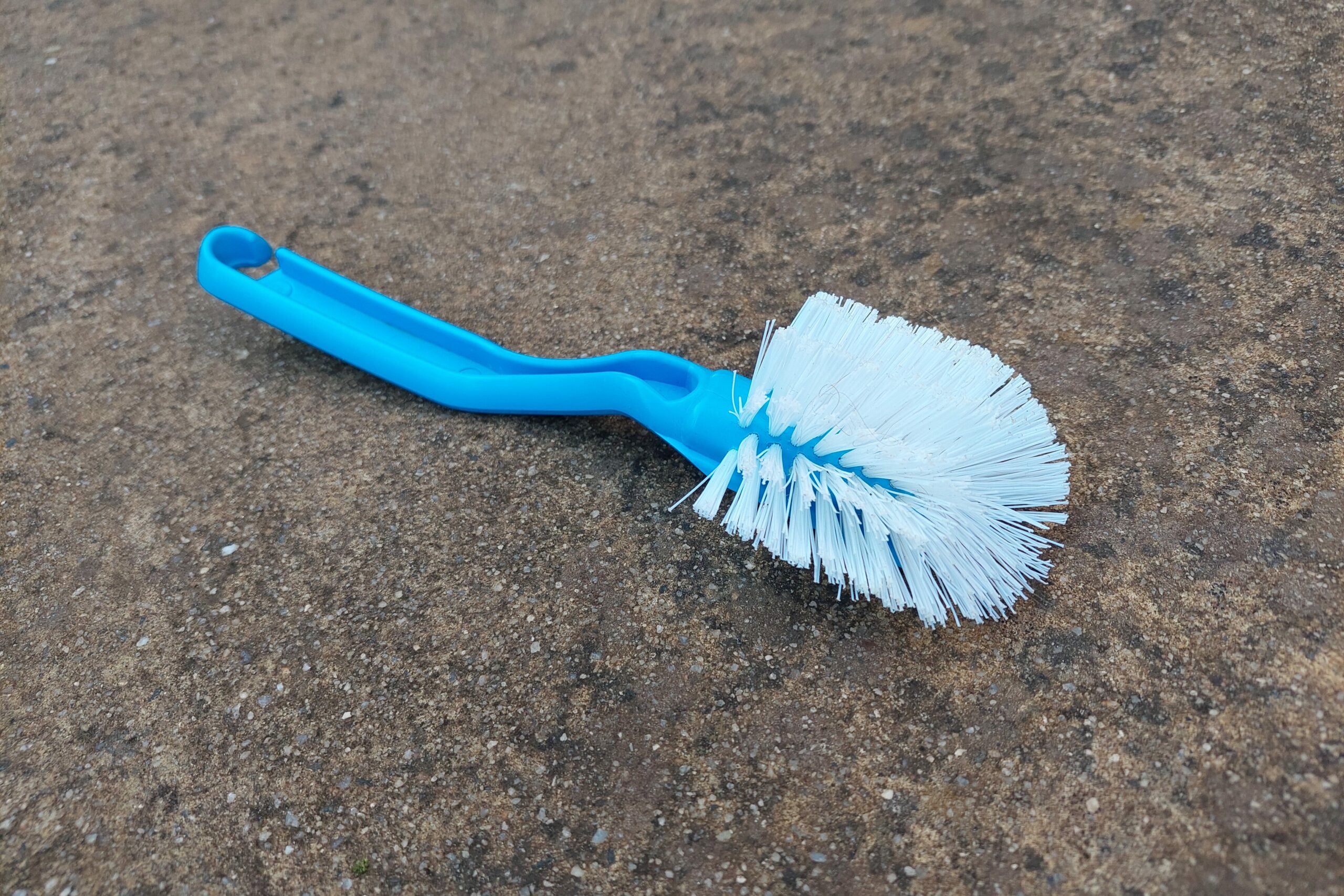 A close up of a blue dish brush on the concrete floor.